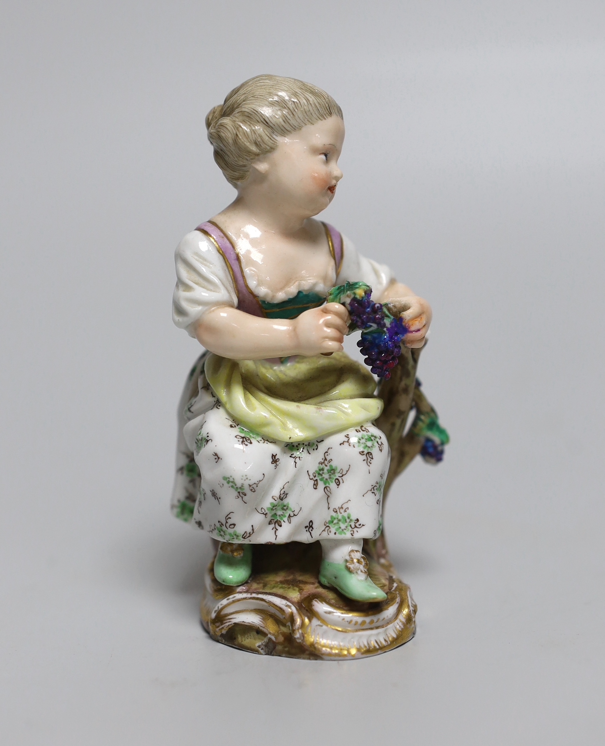 An early 19th century Meissen figure of a girl seated on a tree stump holding a bunch of grapes, painted 58, incised mark and feint crossed swords in blue, 11cm